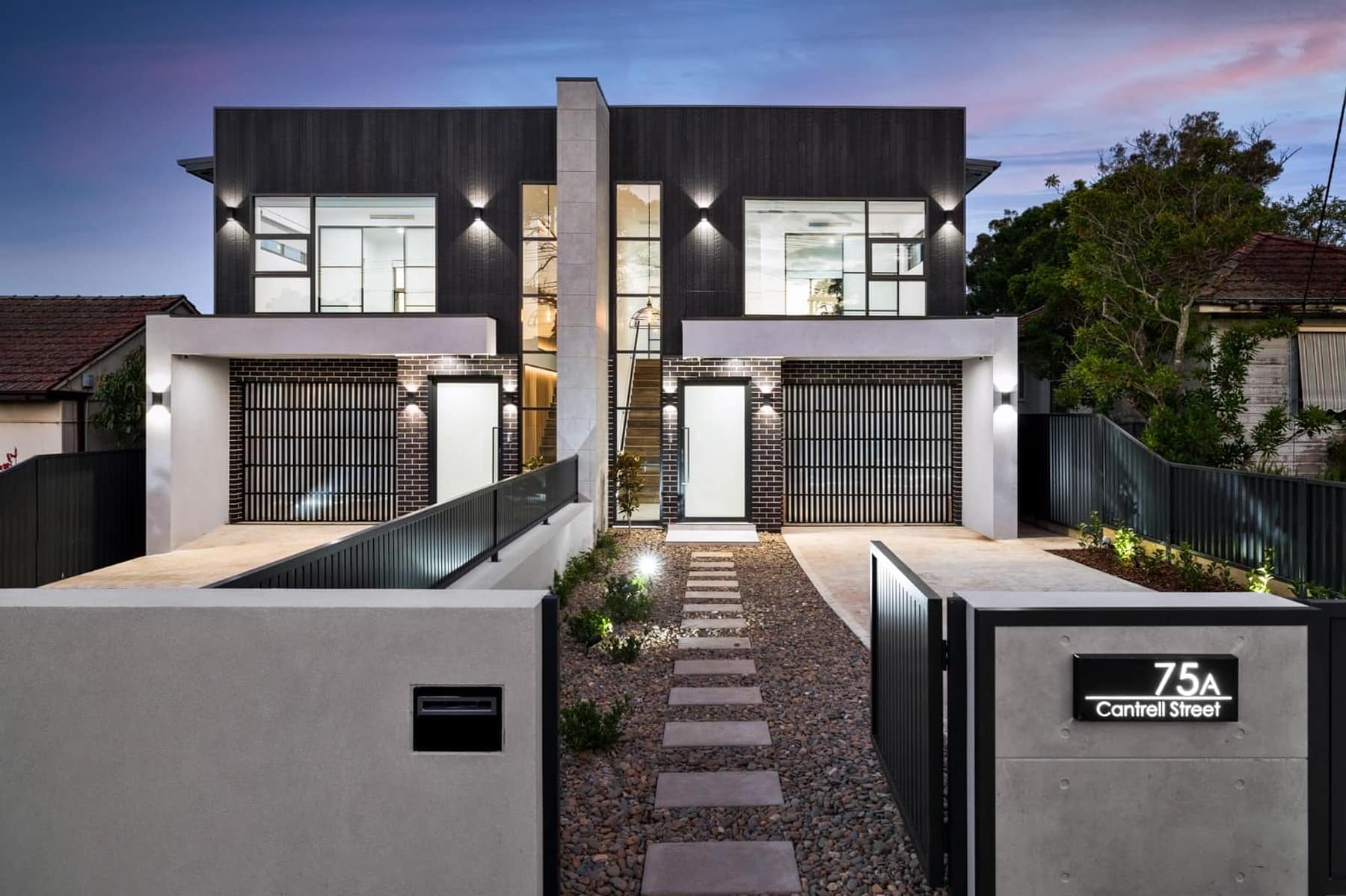Twilight street view of the Cantrell Street duplex pair in Yagoona, with charcoal brick, white render and feature lighting