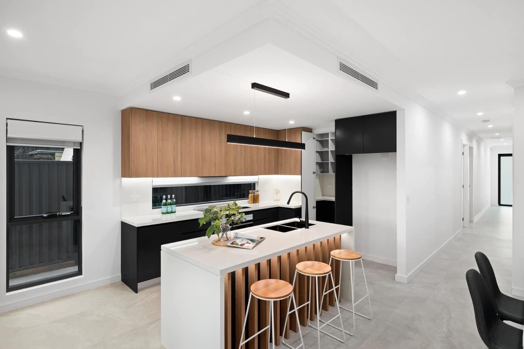 Kitchen with timber overhead cabinetry, stone island bench, timber battens and walk-in pantry
