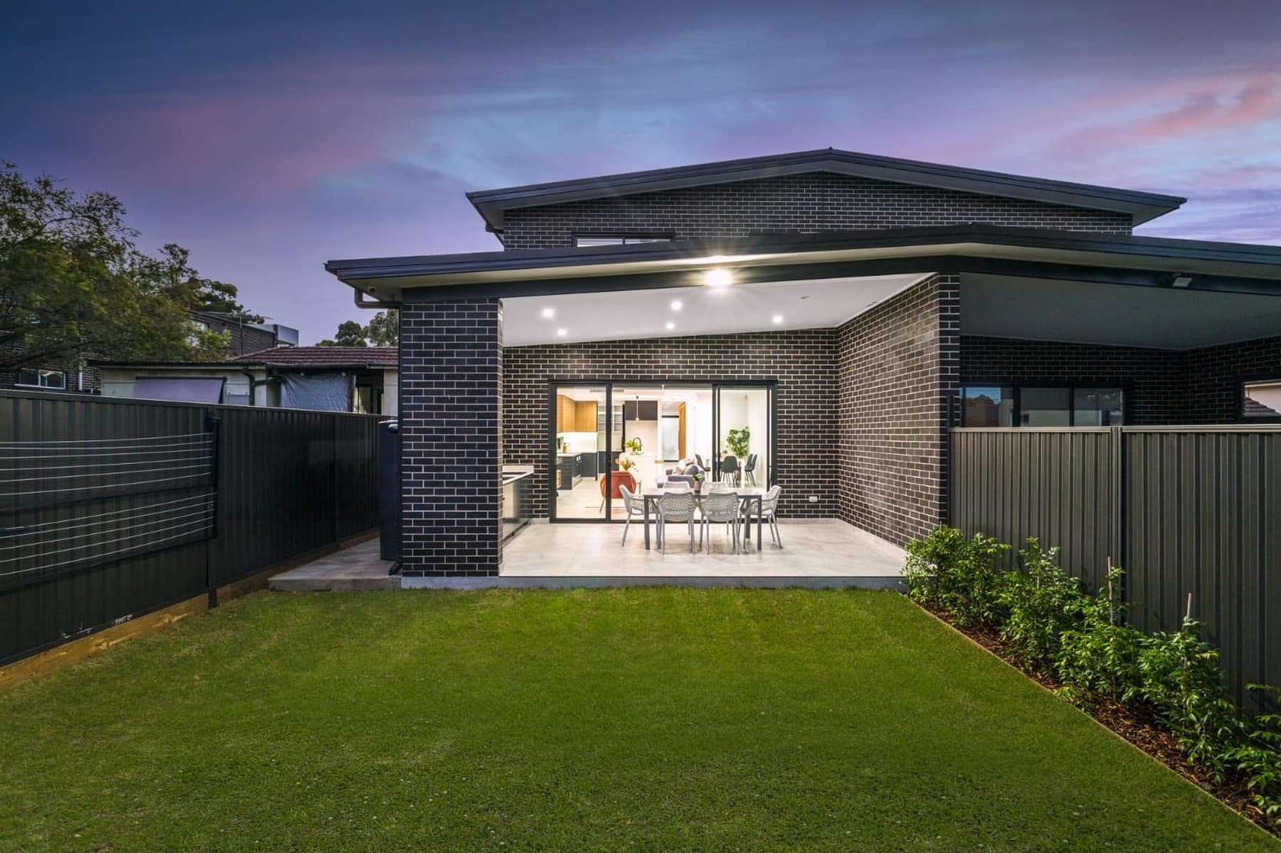Rear elevation at dusk with black brick, wide alfresco opening and level lawn