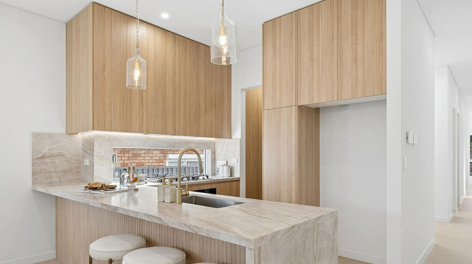 Kitchen with stone benchtops, timber cabinetry and island seating under pendant lighting