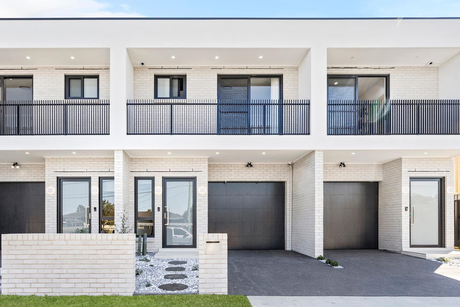 Street view of the four Stockton Avenue townhouses in Moorebank, with white render, balconies and dark garage doors