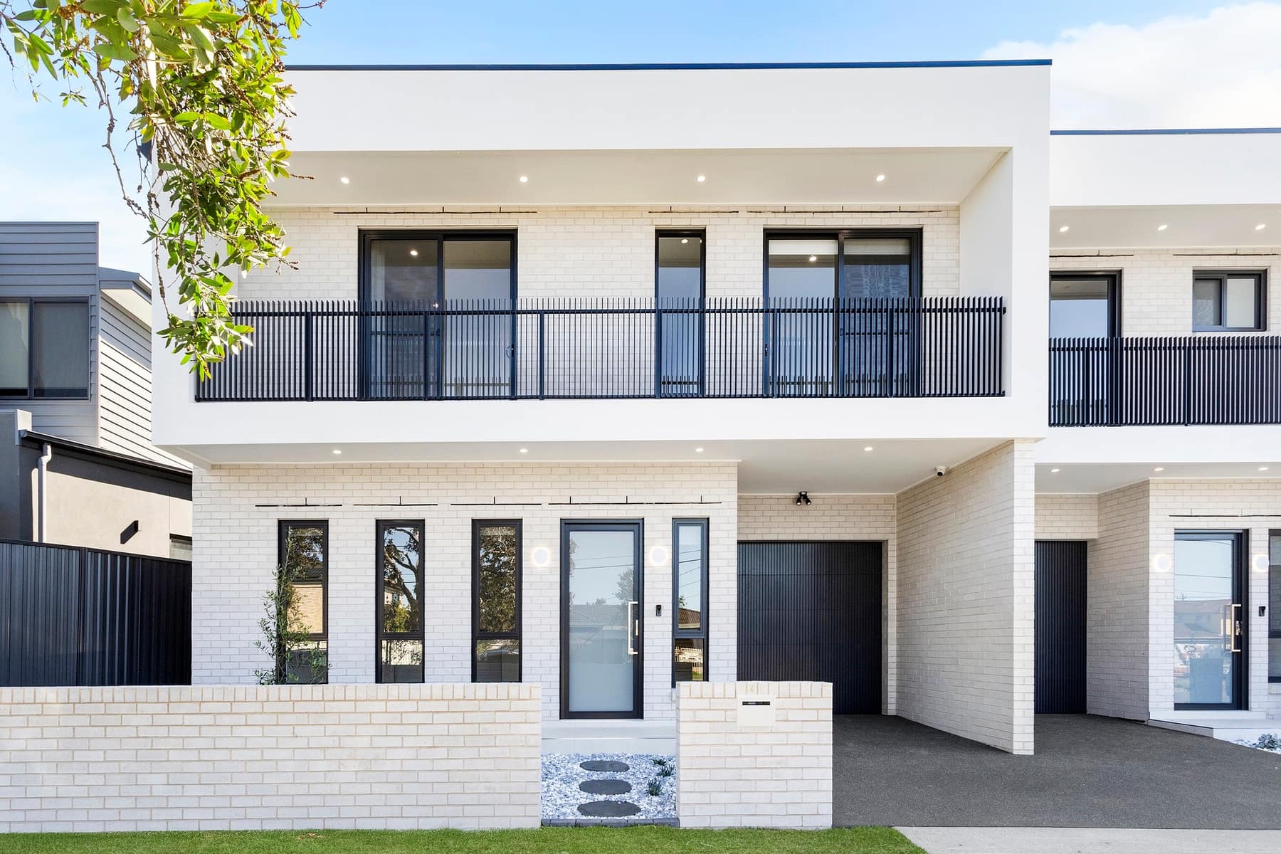 Facade detail of a townhouse pair showing the balcony, garage and landscaped entry